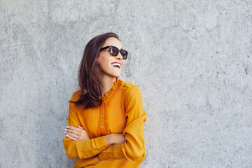 Happy young woman wearing sunglasses looking away standing against concrete wall
