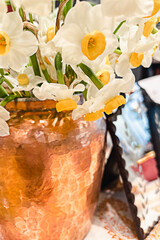 Defocused bouquet of daffodils in an old vintage copper vase standing on a table next to a small mirror.