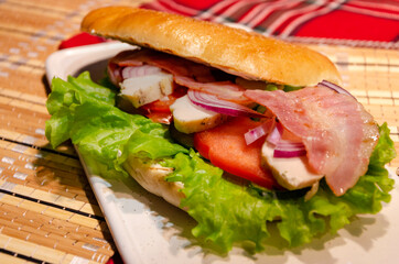 Ciabatta with ham, pieces of meat, tomatoes, onions and lettuce