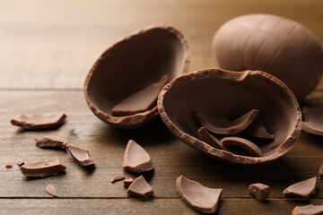Broken and whole chocolate egg on wooden table, closeup