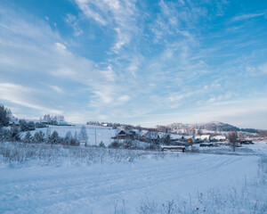 Snow-covered village at the hill on a frosty winter day. Beautiful landscape with village and conifer forest on snowy day.