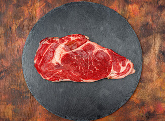Raw beef ribeye on a round slate plate on an old wooden table in brown tones