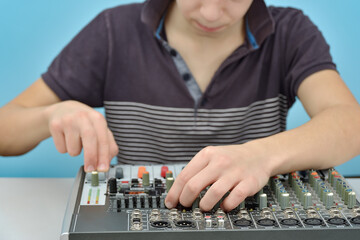 A boy adjusts the equalizer of a mixing console in a music studio.