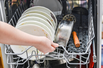 The girl opens the dishwasher to load dirty dishes.