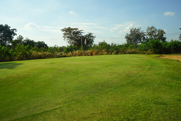 Fototapeta na wymiar Background of evening golf course has sunlight shining down at golf course in Thailand. Nice scenery on a golf course at a late summer afternoon.