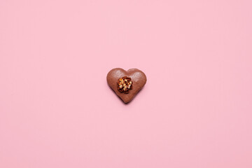One chocolate heart shaped Valentines Day macaron on a pastel pink background with copy space and room for text