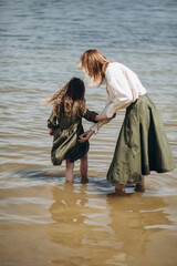 Family vacation by the river in summer. Mom and daughter are standing in the water. Rear view