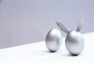 Minimal concept for Easter. Egg with bunny ears colored silver on a white-gray background