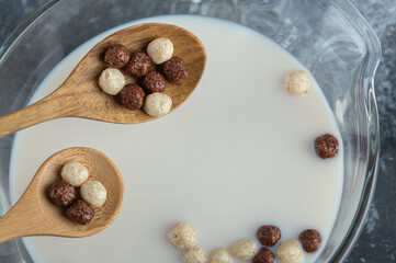 Wooden spoons of cereal balls on top of bowl of milk