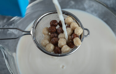Strainer spoon full of cereal balls on top of milk