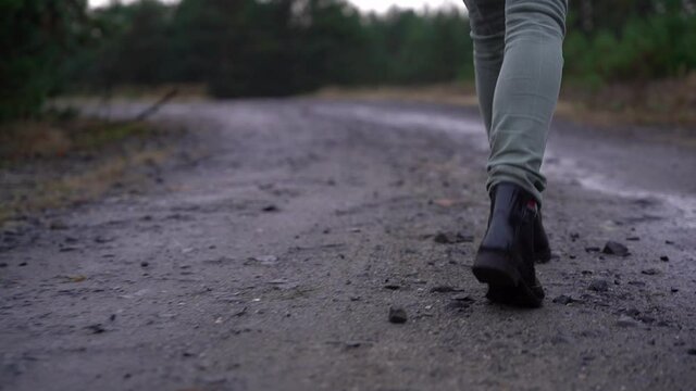 Młoda kobieta idzie po leśnej drodze w kaloszach. Kamera za obiektem. Bliski plan. Zach&oacute;d słońca