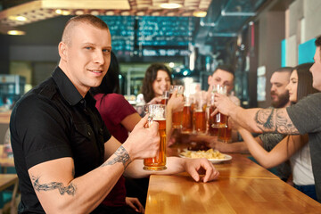 Side view of tattooed man keeping glass of beer in pub