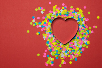 Heart-shaped paper puncher confetti scattered on a red background. Valentine LOVE concept