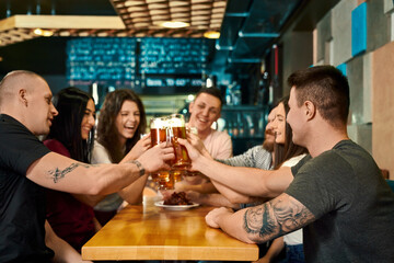 Young friends keeping pints with beer and toasting in pub