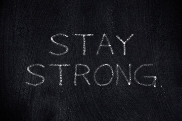 Obraz premium The motivational words Stay Strong, written with white chalk on a rough worn blackboard surface. 