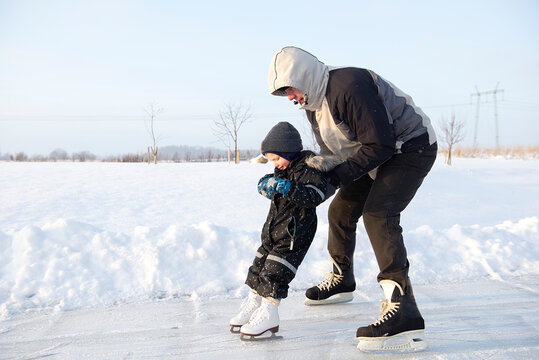 Grandfather teaching her little grandson ice skating at outdoor skating rink.