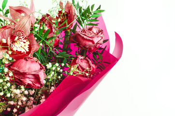 Flower arrangement of red fading flowers orchids and roses in colored paper on a white background close up