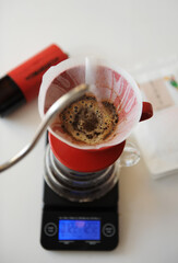 V60 coffee brewing, top view. Red dripper, electronic scales. On white table