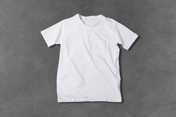 Basic white Tshirt on grey concrete surface. Mock up for branding t-shirt with pocket. 