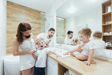 Fototapeta premium Young happy family man, woman and two small children, two boys in a backpack brushing teeth together in the bathroom