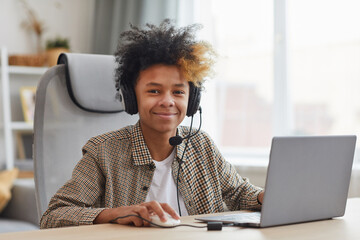 Portrait of smiling African-American boy wearing headset while using laptop at home and looking at...