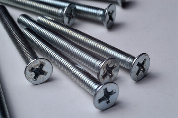 metal screws with a cross-head screwdriver slot lie on a light background. close-up.