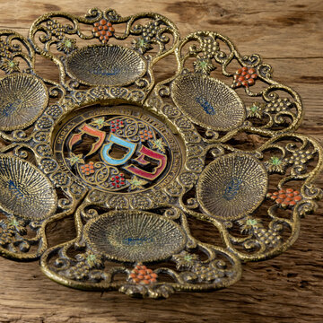 Jewish Passover holiday. Close up of vintage traditional Pesah plate with text in hebrew: Passover, horseradish, celery, egg, bone, maror, charoset. Selective focus.