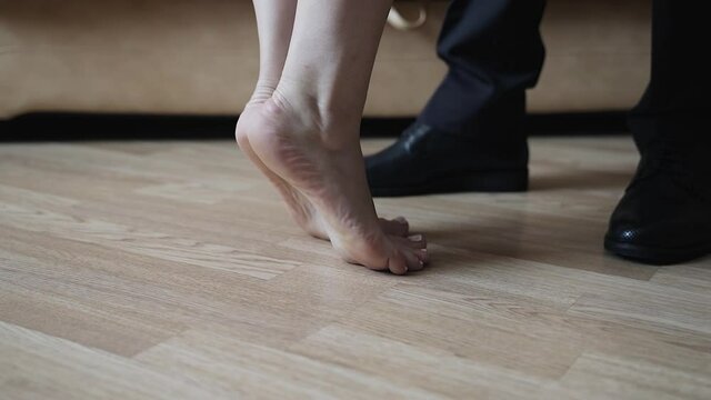 The girl stands barefoot on her toes in front of her boyfriend. Close-up of lovers ' feet