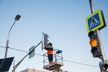 Worker on the lift sets and adjusts the traffic light at the pedestrian crossing