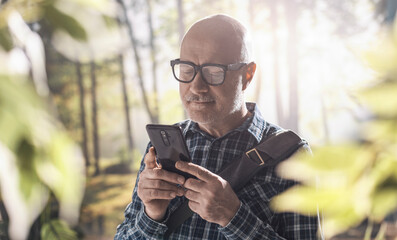 Happy man connecting in the forest with his smartphone
