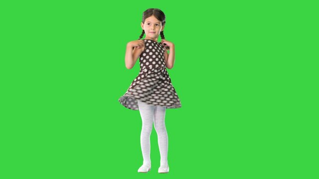 Smiling little girl posing and twirling her polka dot dress on a Green Screen, Chroma Key.