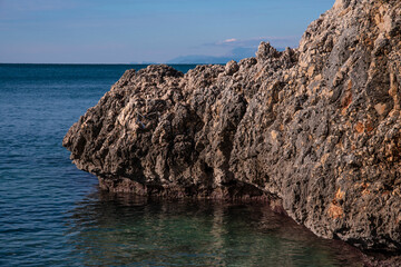 Sea coast with rocky cliffs. Seashore near a mountain with rocks and small waves. Stone rock in clear blue water.