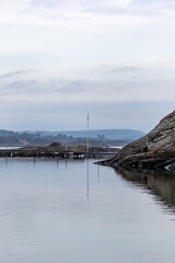 Sea scape on grey day with flag pole and lamp post reflecting in water