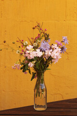 bouquet of wildflowers in the glass carafe. yellow wall as background