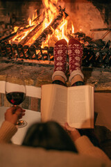 Cosy winter evening. Drinking wine and reading book next to fireplace.