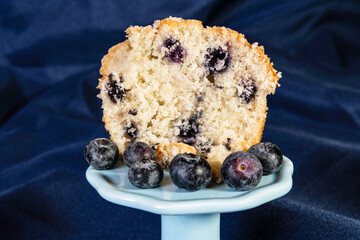 half a blueberry muffin with fresh blueberries on blue