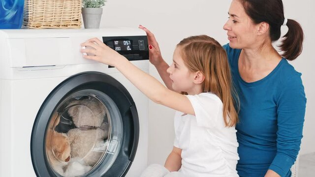 Mother teaching daughter how to operate washing machine at home