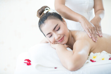 Female spa staff doing salt spa for Asian women. Young Asian woman having exfoliation treatment with body scrub in spa salon.