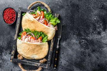 Doner kebab with grilled chicken meat and vegetables in pita bread on a wooden tray. Black background. Top view. Copy space - obrazy, fototapety, plakaty