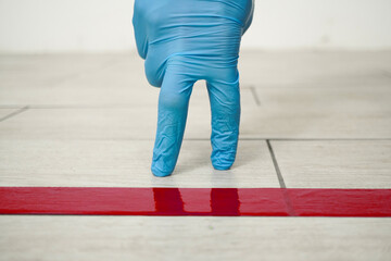 Walking hand is standing in line behind red tape floor marking for social distance indoors, close up. Social distancing for coronavirus prevention. Covid-19 pandemic concept.