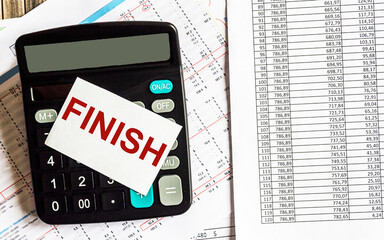 The word FINISH is written on the calculator display. There are documents with numbers on the table