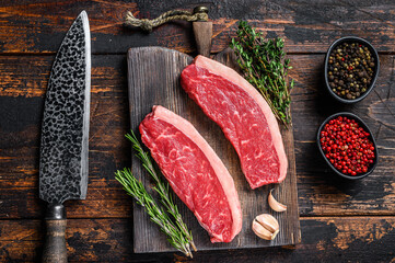 Raw top sirloin beef meat steak on a cutting wooden board. Dark wooden background. Top view