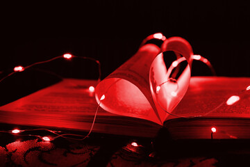 Red art book novel with sheets in the shape of a heart decorated with bright garland lights and highlights in the background, a romantic symbol of love, macro. Valentine day. Greeting card. Close up