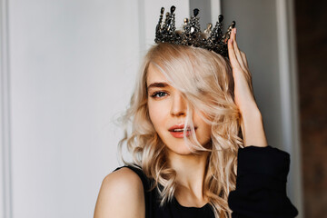 Portrait of a beautiful young blonde woman, wearing a black crown, looking at camera.