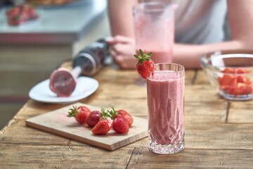 Strawberry smoothie on wooden table in the kitchen. Healthy eating, cooking and summer refreshment concepts.