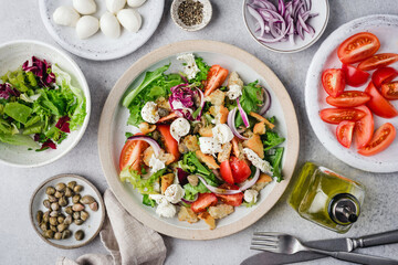 Healthy salad with tomatoes, croutons, greens and mozzarella cheese on a plate. Italian style Panzanella salad with mini mozzarella balls and capers