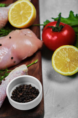 Raw chicken fillet and legs on wooden plate with fresh vegetables. Close up