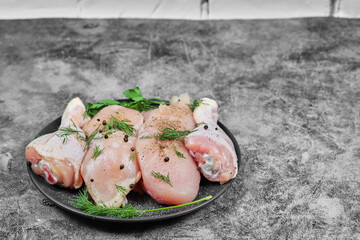 Raw chicken meat slices on black plate with chopped greens