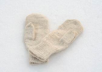 White female woolen mittens on white snow. Winter clothes.