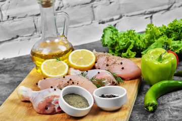 Raw chicken fillet and legs on wooden plate with fresh vegetables, spices and glass of oil